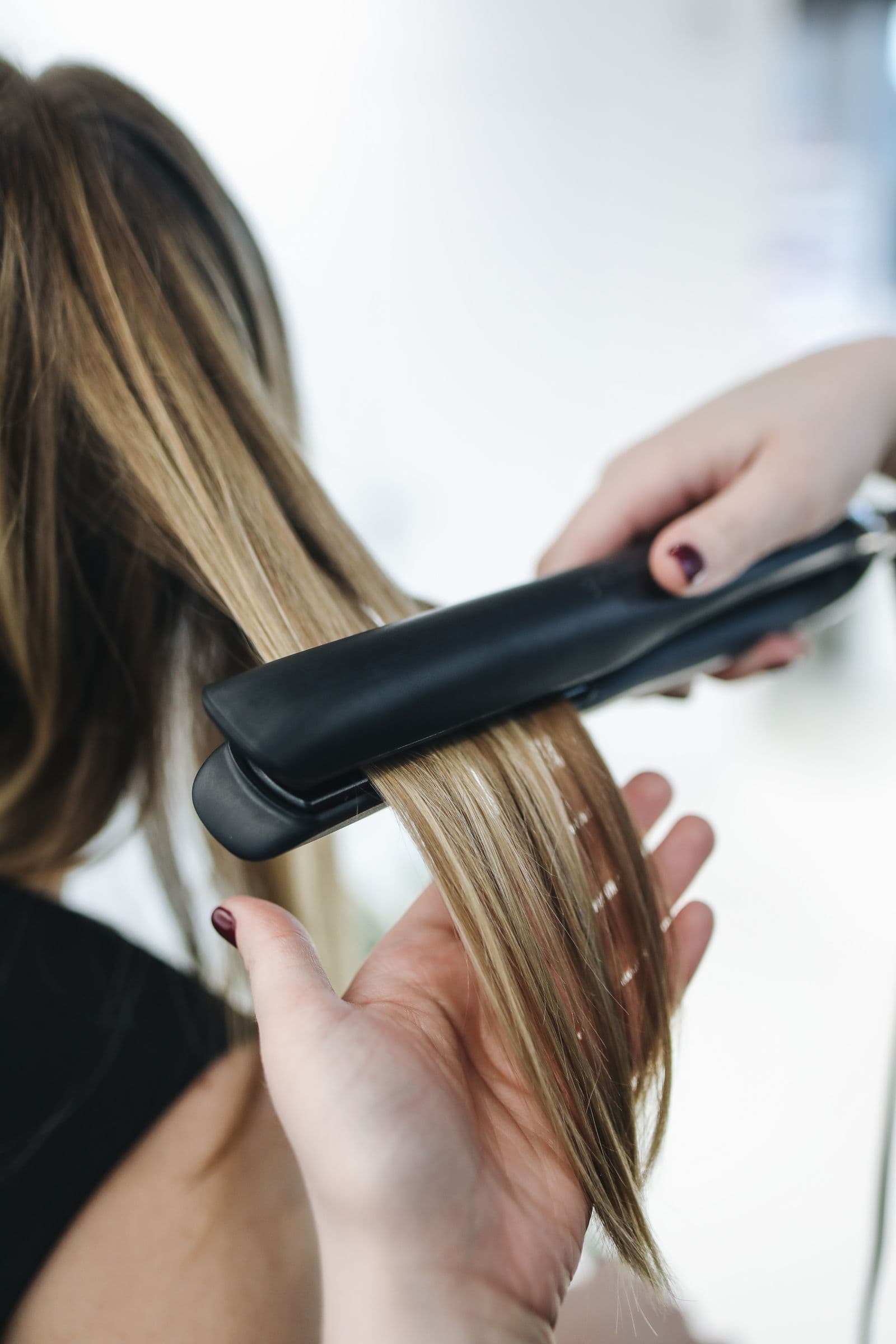 Frizerka z likalnikom gladi pramen svetlih las v salonu
